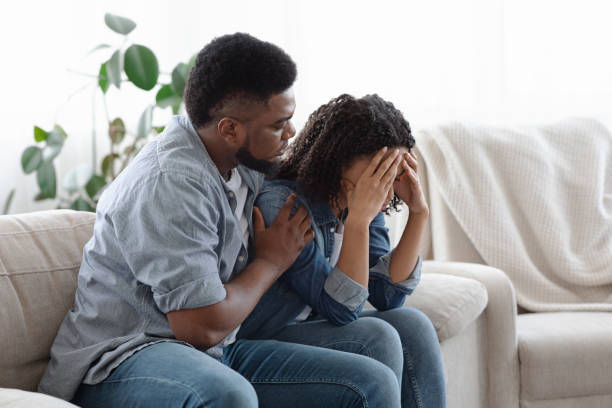 Dependent Relationship. Young Black Guy Soothing His Depressed Girlfriend At Home Dependent Relationship Concept. Young Black Guy Soothing His Depressed Girlfriend At Home, Embracing Her On Couch In Living Room symbiotic relationship stock pictures, royalty-free photos & images