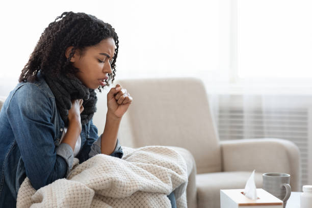 Risk Of Coronavirus. Sick Black Woman Coughing Hard At Home Risk Of Coronavirus. Sick Black Woman Coughing Hard At Home, Sitting On Couch Wearing Scarf And Covered With Blanket, Side View With Copy Space coughing stock pictures, royalty-free photos & images