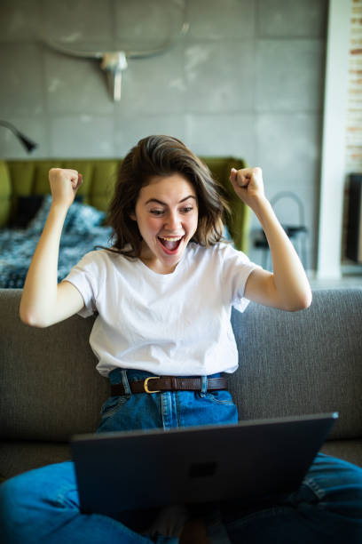 istock Joyful woman with win gesture using laptop on the sofa 1227312349