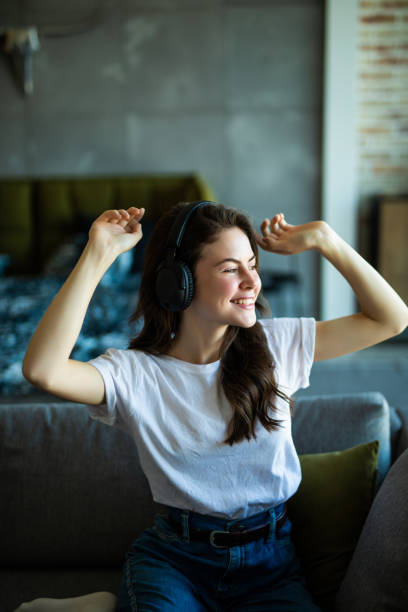 istock Young cute smiling woman dancing on couch while using wireless headphones at home 1227313816