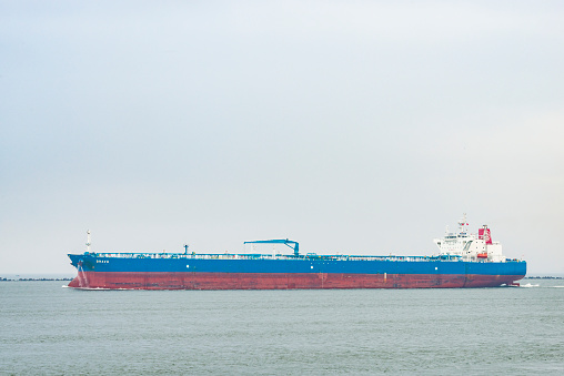 Large oil tanker ship Bravo leaving the port of Rotterdam on an overcast day. The ship is sailing out of the Nieuwe Waterweg onto the North Sea.
