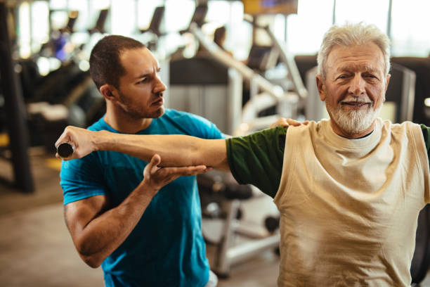 istock Senior man exercising with personal trainer using dumbbells at the gym 1227317568