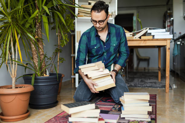 тысячелетний человек, организующий свои книжные коллекции - pile arrangement стоковые фото и изображения