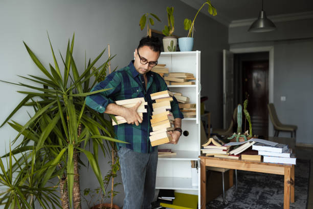 millennial man organizing his book collections - pile arrangement imagens e fotografias de stock