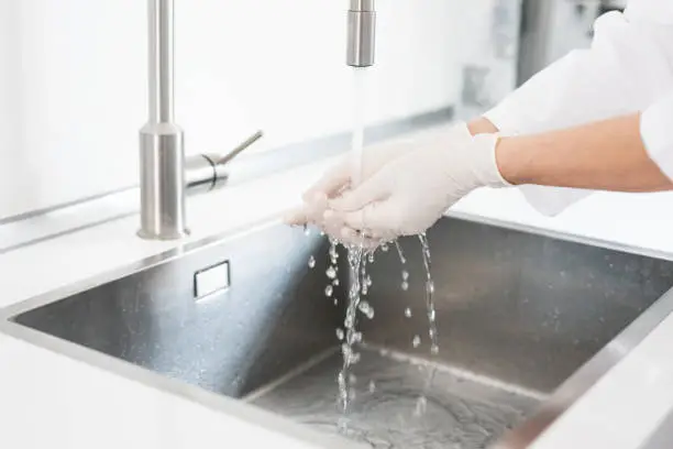 Woman with doctor's coat and latex gloves washes her hands, topic hygiene