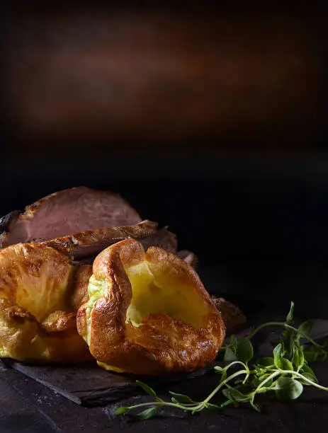 Traditional British Yorkshire puddings served with prime roast beef and thyme herb garnish. Shot against a rustic background with copy space.