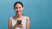 アジアの幸せな美しい女性ブロガーは、笑顔で、コピースペースで青い色の背景に隔離されたスマートフォンを保持しています。オンライン技術マーケティングのコンセプト。
