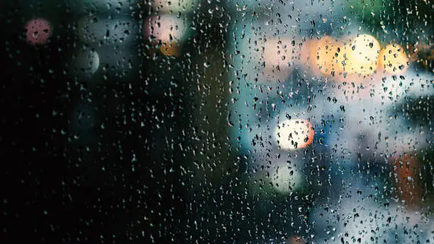 Photo of Window and rain drop in condominium or apartment room on a rainy day in Bangkok Thailand and background outside is blurred bokeh of raining city light and natural tree and sky.