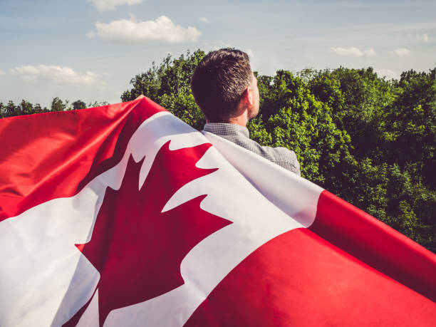 Attractive man holding Canadian Flag. National holiday Attractive man holding Canadian Flag on blue sky background on a clear, sunny day. View from the back, close-up. National holiday concept canada flag blue sky clouds stock pictures, royalty-free photos & images