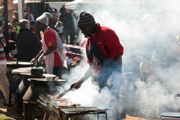 Male chef vendor working a BBQ Grill at hotdog stall at farmer's market Johannesburg, South Africa - June 7, 2014: Male chef vendor working a BBQ Grill at hotdog stall at farmer's market south african braai stock pictures, royalty-free photos & images