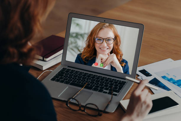 View over shoulder of female freelancer talks with employee by video call, discuss strategy of work. Laptop screen view of smiling ginger woman in spectacles. New technology usage. Distance working ver sobre el hombro de las conversaciones de mujeres freelancer con empleado por videollamada, discutir la estrategia de trabajo. vista de pantalla portátil de mujer de jengibre sonriente en gafas. uso de nueva tecnología. trabajo a distancia