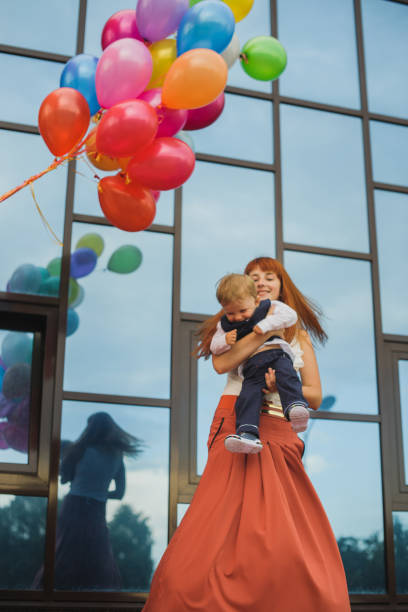 femme tenant un bébé dans ses bras, la joie et le plaisir, des ballons de différentes couleurs - single mother one parent child kissing photos et images de collection