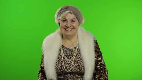 Elderly style granny caucasian woman posing on chroma key background. Portrait of old stylish grandmother in retirement age in fashion clothing. Place for your logo or text. Green screen