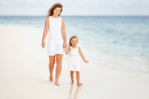 Mother and little daughter walking on beach on Maldives at summer vacation