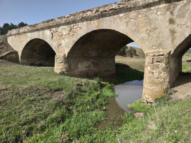 istock Old soviet bridge made of stone. Little gray river. Green grass. Blue sky 1227346858