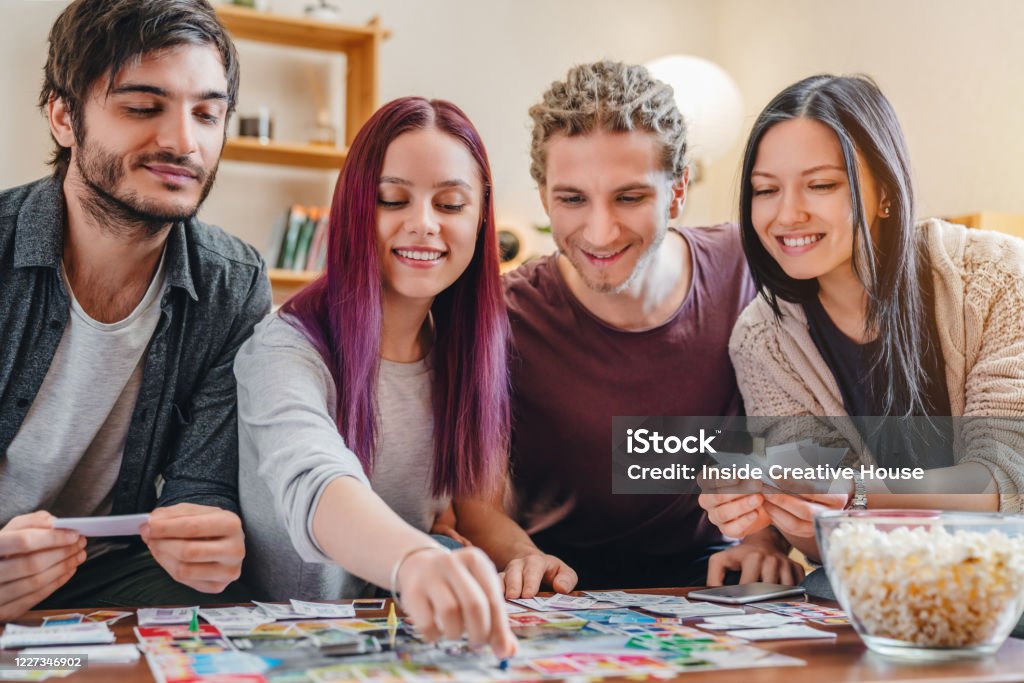 Young group of friends playing board game on table at home interior People, Fun, Domestic Life, Lifestyles, Weekend Activities Board Game Stock Photo