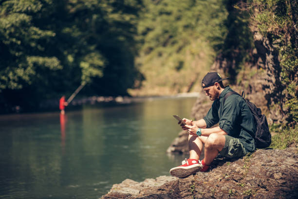 istock Single male hiker using tablet on nature while sitting on rocky river shore 1227347265