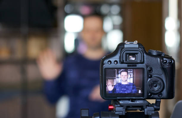 A blogger takes himself on camera. In focus is his camera and the image on it. Gesture of greeting. Everything else is blurry.
