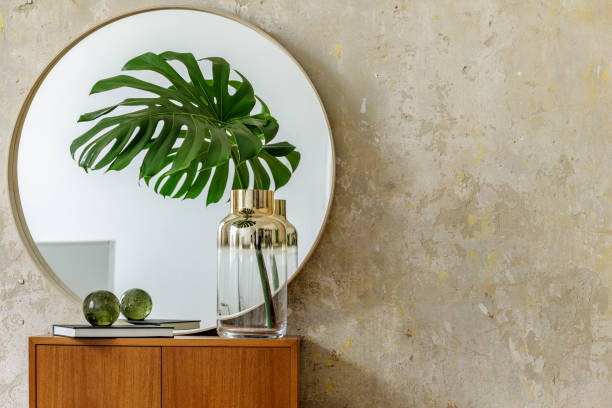 istock Minimalistic composition at modern retro interior with design commode, tropical leaves in vase, round mirror, copy space, book, grunge wall and elegant accessories in stylish home decor. 1227350023