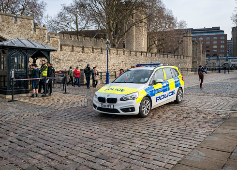 A Metropolitan Police car driving slowly past the visitors’ entrance to the Tower of London. A few tourists are wandering on the Embankment or queuing to enter the Tower, one of London’s most popular tourists attractions.