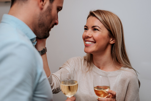 Smiling couple drinking white wine and cuddling. Close-up.