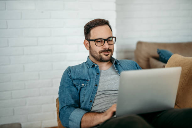 istock Handsome man in casual clothes using laptop while relaxing at home, portrait 1227355422