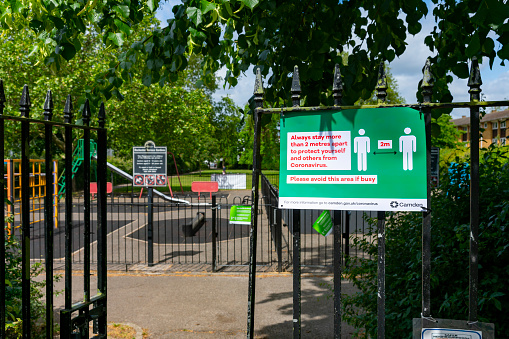 Social distancing reminder on the gate to a park in Camden, North London, UK.
