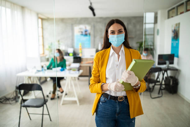Portrait of female bank manager with protective face mask in office Portrait of female bank manager with protective face mask and surgical gloves in office, standing, looking at camera and smiling during covid-19 pandemic resilience photos stock pictures, royalty-free photos & images