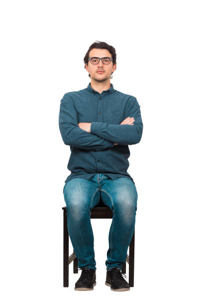 自信に満ちたビジネスマンの完全な長さの肖像画は、椅子に座って眼鏡をかけ、腕を組み、白い背景に隔離し続けます。カメラに決心した、満足のいくビジネスパーソン。 - determination isolated on white vertical looking at camera ストックフォトと画像