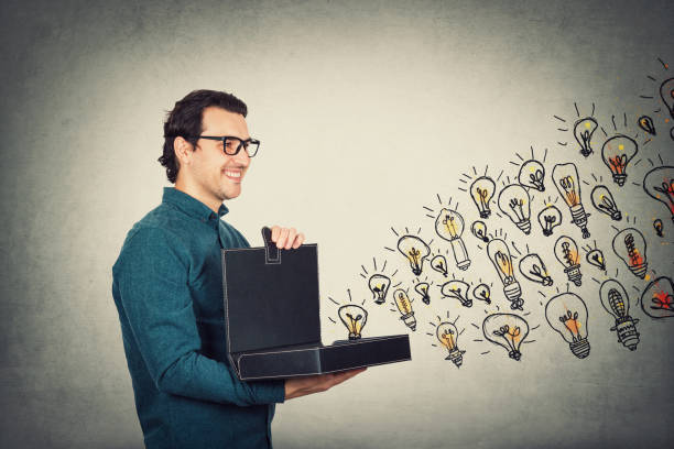 istock Businessman opens his briefcase filled with brilliant ideas as different lightbulbs comes out of the box. Ingenious boss shows the business portfolio, shares his creativity and genius with employees. 1227365513