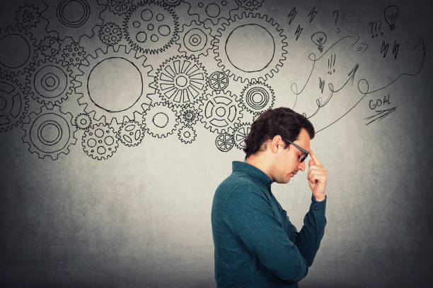 istock Wistful businessman, keeps index finger to forehead, hard thinking. Different gear cogwheels as metaphor of brain working as a whole mechanism. Search for solutions in mind. Deliberation concept. 1227365837