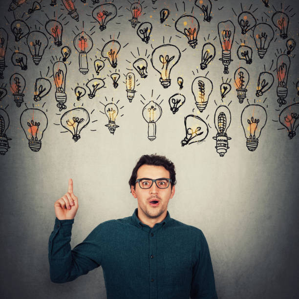 istock Astonished businessman, looking big eyes to camera, pointing up index finger as multiple lightbulbs float above his head. Surprised business worker, wearing glasses, shows upwards. Brilliant ideas. 1227366785