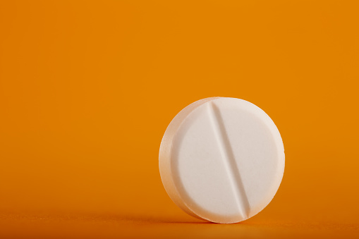 White round medical pill on yellow / orange background