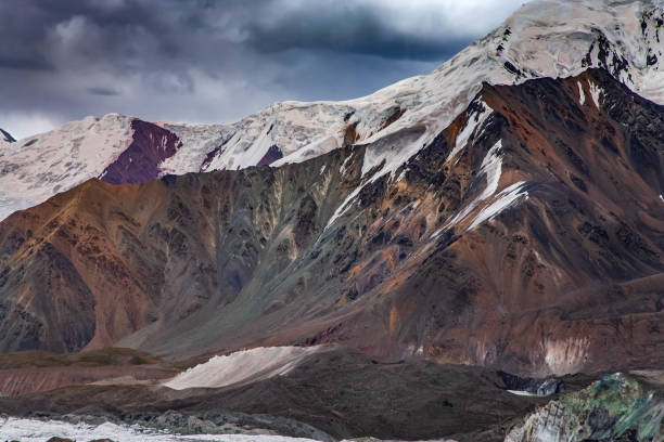 Beautiful mountainious landscape. Scenic view of snowy mountain peaks and hilly valley in front of it. Cloudy sky.