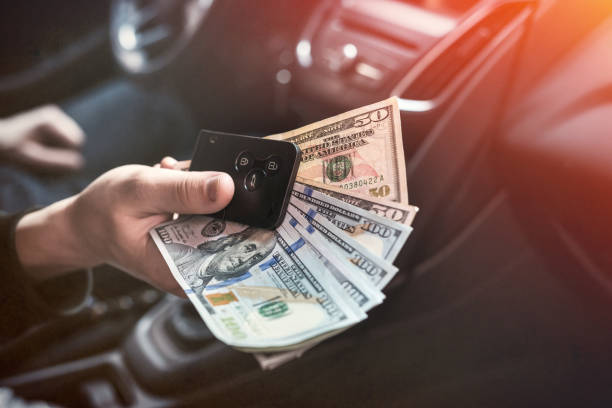 istock dollar and car key in male's hand inside car 1227368149
