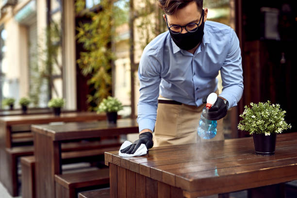 Preparing for the customers after reopening! Waiter wearing protective face mask while disinfecting tables at outdoor cafe. new normal concept stock pictures, royalty-free photos & images