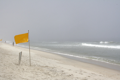 Flag on the beach indicating danger, landscape with many clouds. Taken by iPhone 13 Pro Max. Edited in Adobe lightroom and Adobe Photoshop.