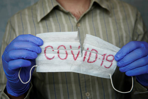 istock removing mask, quarantine ends. Covid-19 background. Stop spread and eliminate Coronavirus. Pandemics. Hands in blue medical gloves tearing the mask with covid-19 print. getting out of isolation 1227371824