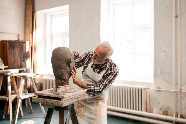 senior mann macht statue aus ton formung eines gesichts mit arbeitswerkzeug - künstlerischer beruf stock-fotos und bilder