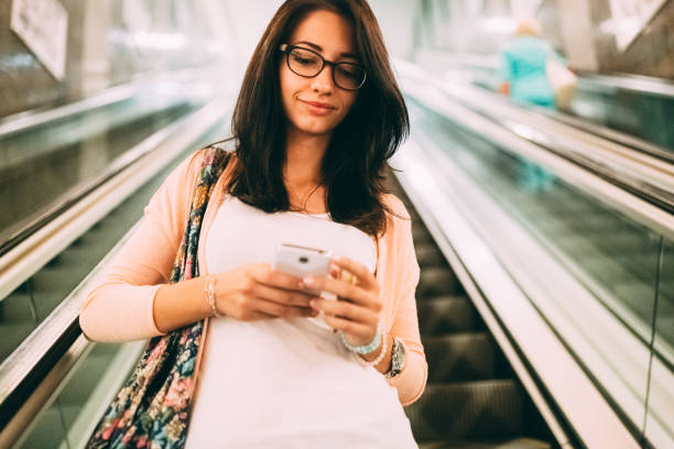 istock Young woman traveling on escalator is using phone 1227374049