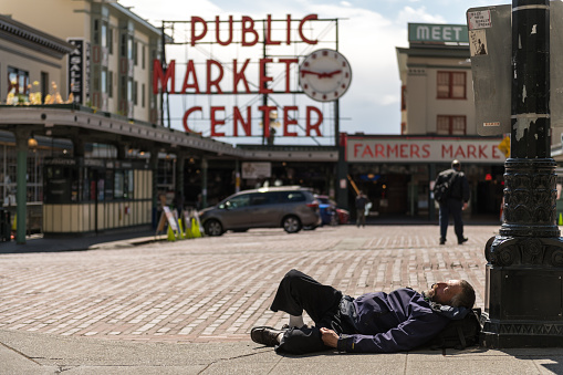 Seattle, USA - May 3, 2020: Late in the day during the stay at home a man sleeping on the sidewalk by pike place market during the covid-19 pandemic.