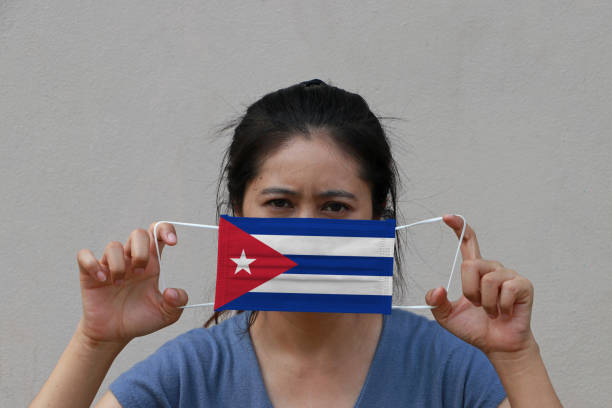 una donna con bandiera cubana su maschera igienica in mano e sollevò la faccia anteriore su sfondo di colore beige. piccola protezione da particelle o virus corona o covid 19. - arms lifted foto e immagini stock