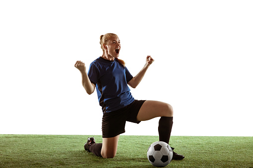 Young female soccer or football player with long hair celebrating goal, winning with expressive emotions on white studio background. Concept of healthy lifestyle, professional sport, motion, movement.