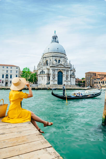 woman in yellow sundress sitting on pier with view of grand canal woman in yellow sundress sitting on pier with view of grand canal Venice Italy summer vacation time. copy space venice stock pictures, royalty-free photos & images