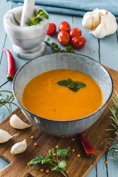 Delicious coloured lentil cream-soup with herbes, tomatoes, chili and garlic lying on a grey wooden table