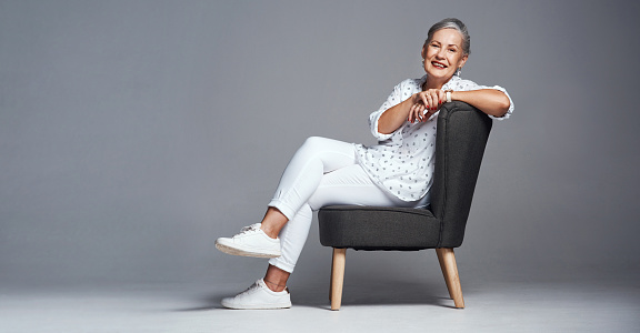 Studio shot of a senior woman sitting on a chair against a grey background