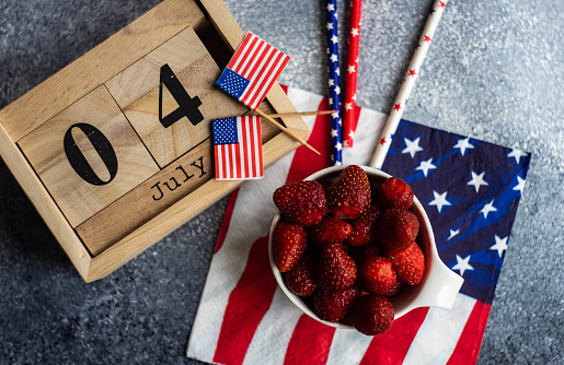 4th July celebration card concept with fresh strawberries and festive stuff on grey background with copy space