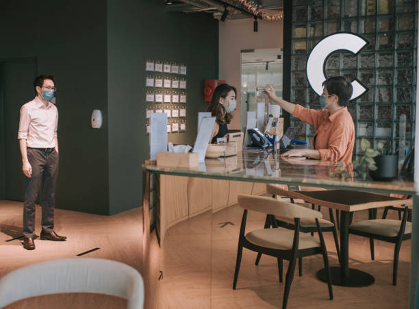 istock an Asian Chinese receptionist conducting standard operating procedure for illness prevention by measuring visitors colleague coworkers body temperature and record their personal data 1227389488