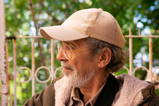 profile of a Middle eastern male with white beard wearing a baseball cap and glasses
