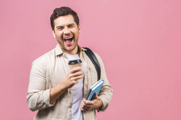 young man with backpack holding coffee cup and tablet computer isolated on pink background. smiling student portrait. studio shot of cheerful men going on travel. - travel ipad isolated backpack imagens e fotografias de stock